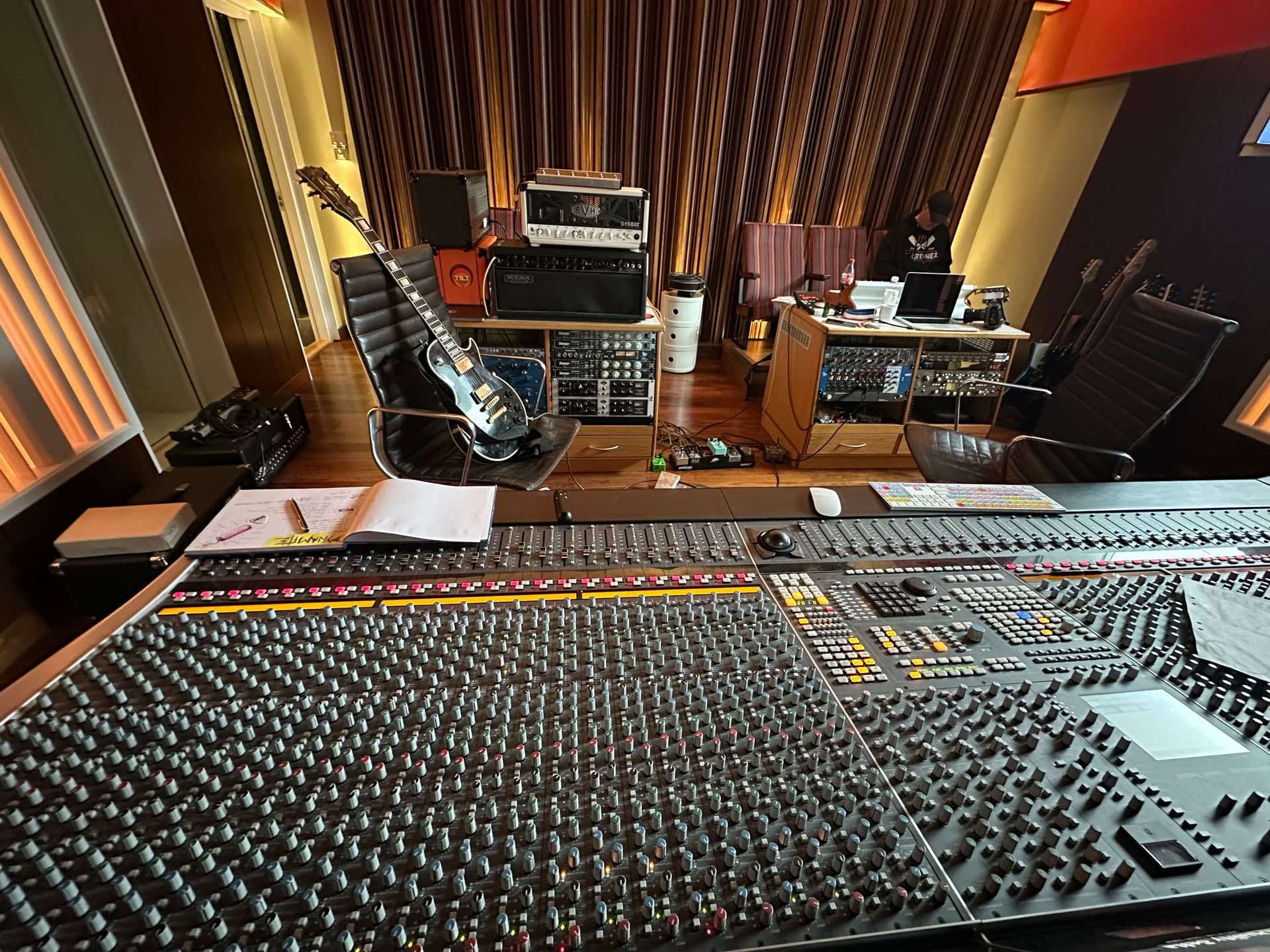 Recording studio control room with a large mixing console, outboard gear, and guitars — where the music is made.