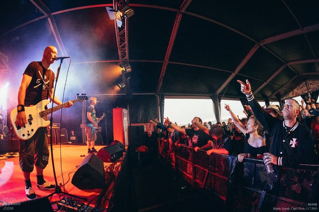 DOMI live on stage under warm orange lights, bassist at the front and a packed crowd at the barrier.